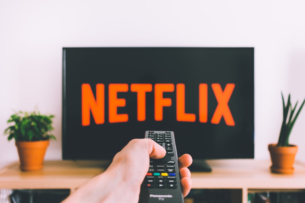 Hand holding a remote control in front of a TV, illustrating the steps for installing an IPTV application.